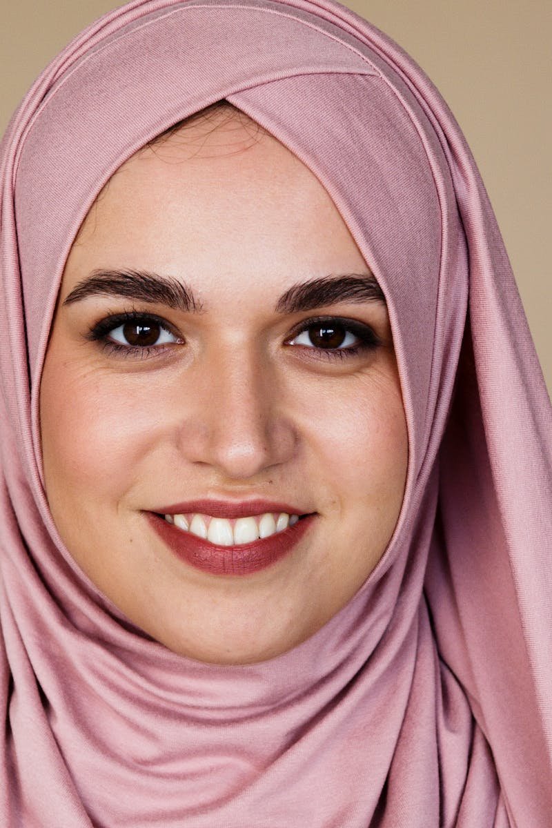 Portrait of a smiling woman wearing a pink hijab against a neutral background.